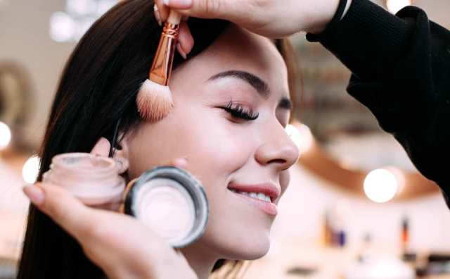 Femme souriante pendant que quelqu'un applique du maquillage sur sa joue.